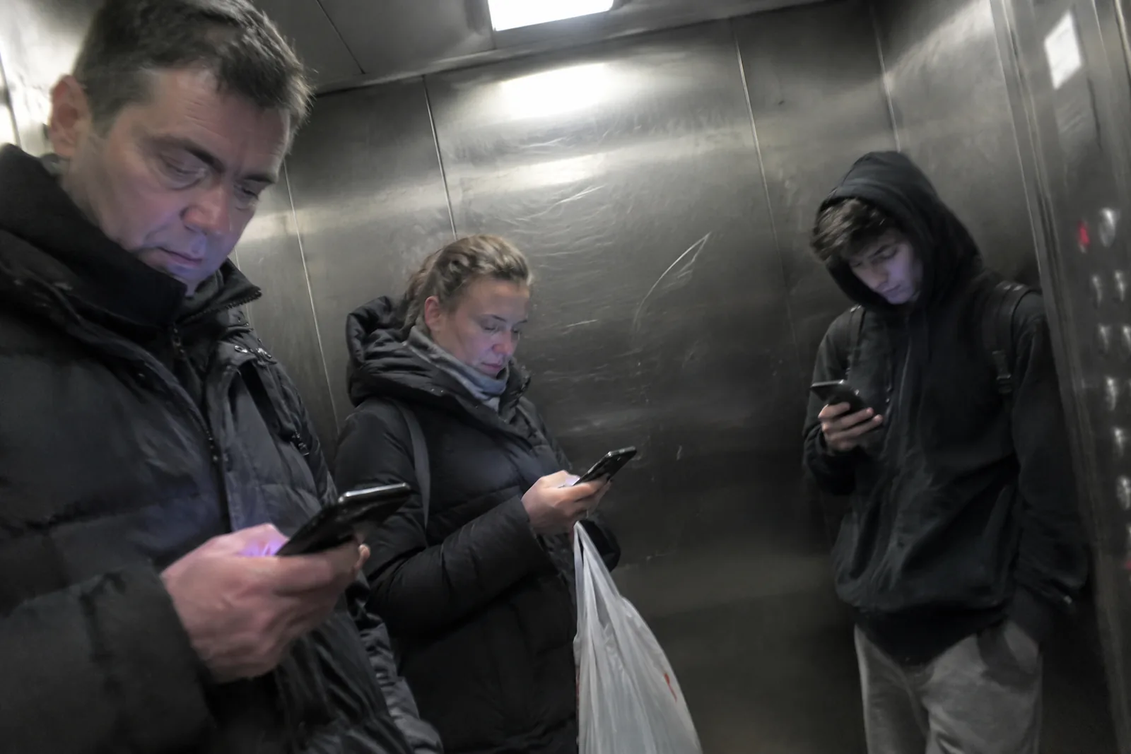 Три человека в лифте молча смотрят каждый в свой телефон